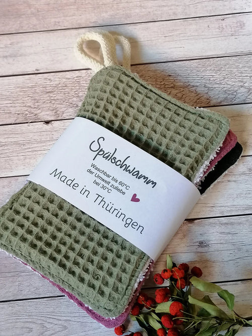  grün, blau  und rosafarbene Spültücher mit Waffelstruktur und die Rückseite ist Frottee zum aufhängen ein kleine Kordel . Die Spültücher haben ein weißes Etikett mit der Aufschrift "Spülschwamm Waschbar bis 60°C der Umwelt zuliebe bei 30°C Made in Thüringen".
